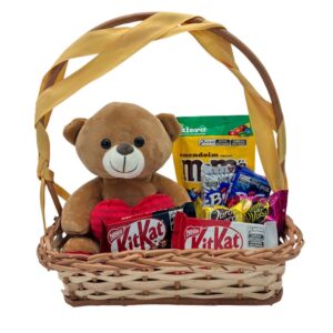 Cesta de palha com laço, pelúcia de ursinho, kit kat, bis e doces variados fundo branco