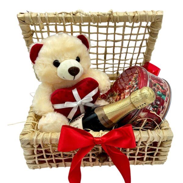 CEsta palha com pelúcia de ursinho segurando coração, espumante chandon e caixa de biscoito amenteigado natal vista frontal